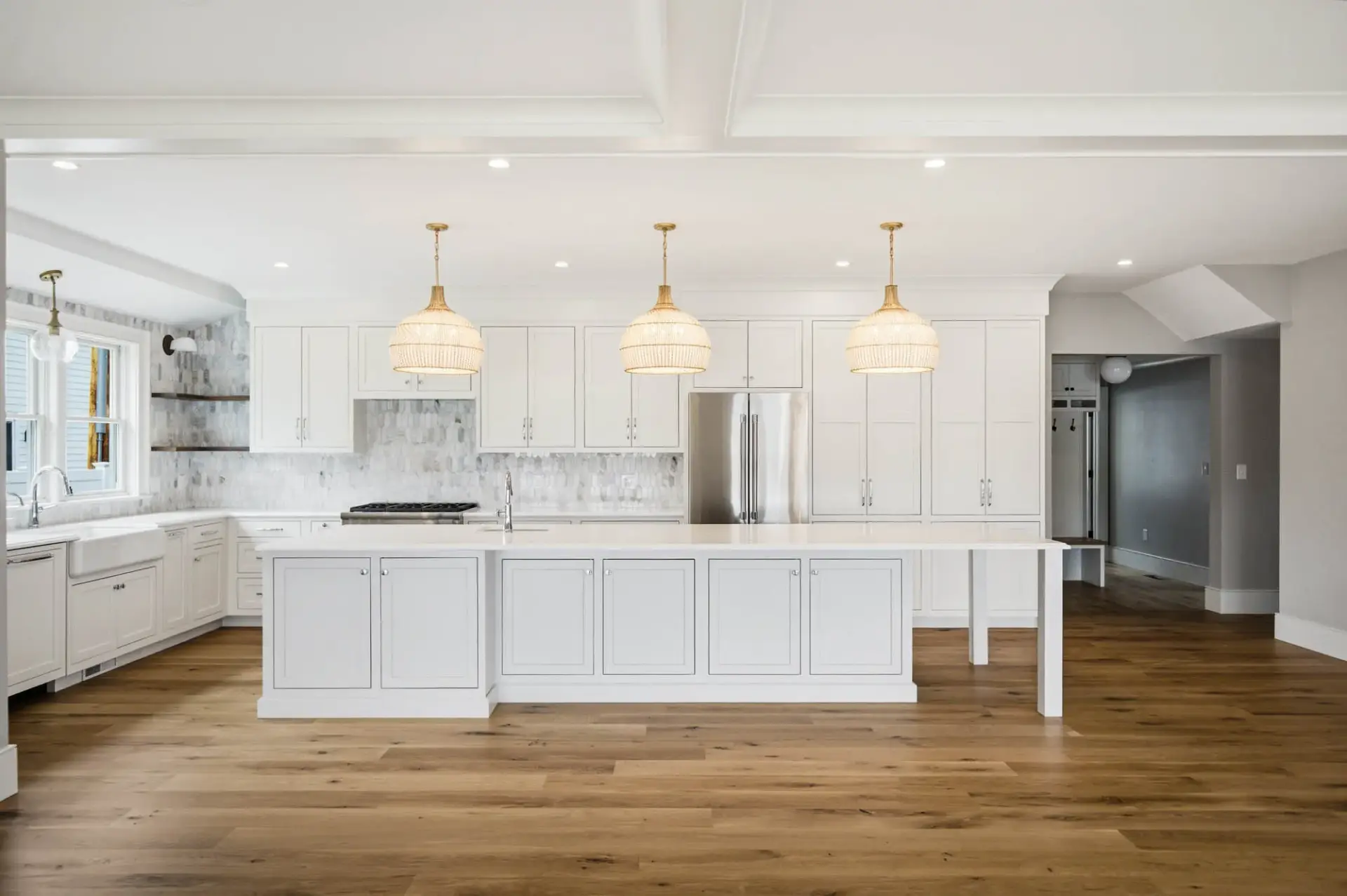 Modern kitchen with white cabinetry, pendant lights, and hardwood flooring.